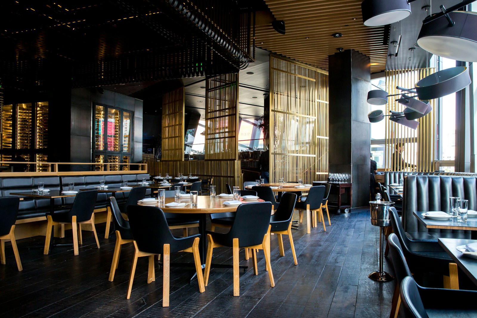 Salle de restaurant contemporaine — banquettes noires, bois et lumière dorée